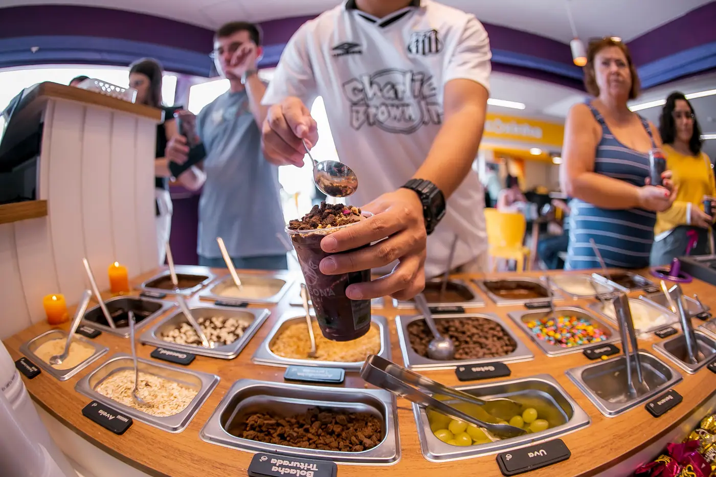 Cliente montando o açaí no balcão de complementos de uma loja Casona